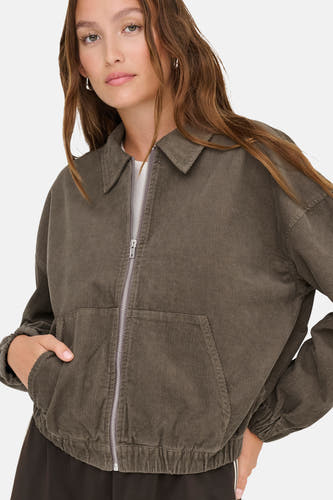 Bruine korte jas van ONLY, met lange mouwen, ritssluiting en zakken, gedragen met een wit shirt.
