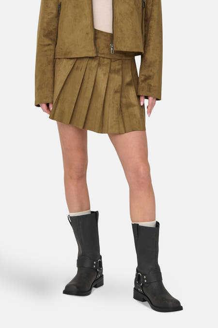 Jupe courte brune de ONLY® à plis, associée à un manteau en suède et des bottes noires.