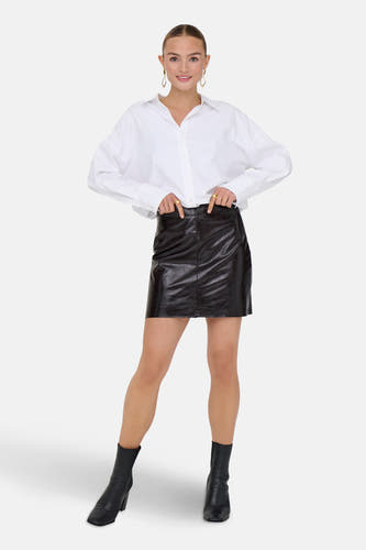 Jupe brune courte de JDY, avec une texture brillante et associée à un chemisier blanc et des bottes noires.