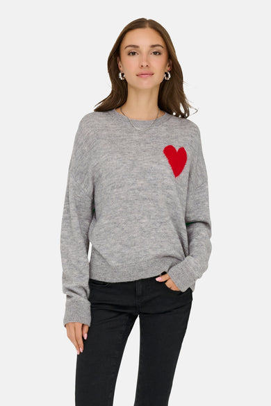 Grijze trui met ronde hals van JDY, met rood hartdetail en gedragen met een zwarte jeans en zilveren sieraden.
