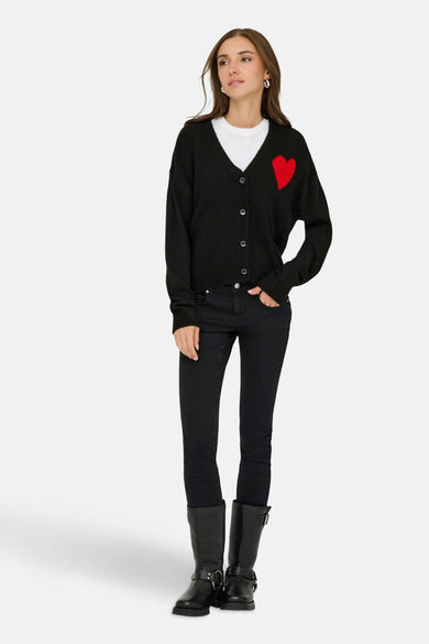 Veste noire de JDY, portée avec une décoration de cœur rouge sur un T-shirt blanc, associée à des jeans noirs et des bottes.