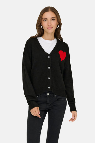 Cardigan noir de JDY, avec des manches longues et une application de cœur rouge, porté sur un T-shirt blanc et des jeans noirs.