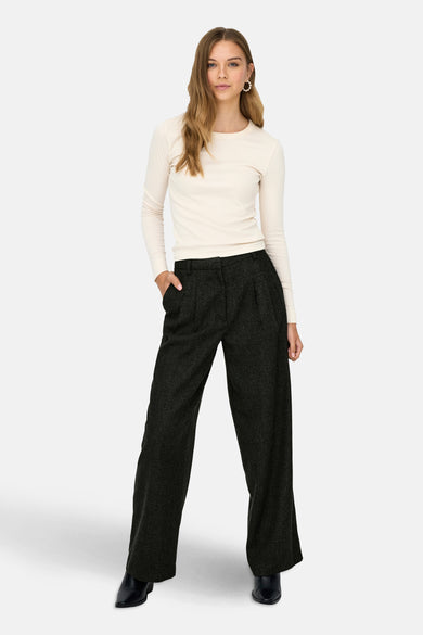 Grijze broek van JDY, met wijde pijpen en steekzakken, gedragen met een crèmekleurige top en zwarte laarsjes.
