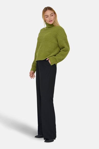 Groene coltrui van ONLY, met lange mouwen en een grove gebreide textuur, gecombineerd met zwarte, wijd uitlopende broek.
