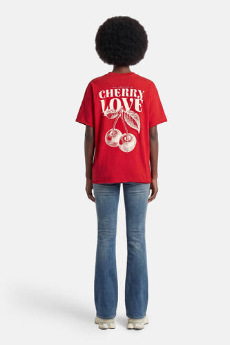 T-shirt rouge à manches courtes de ONLY, avec imprimé blanc 'Cherry Love' au dos, porté avec un jean.