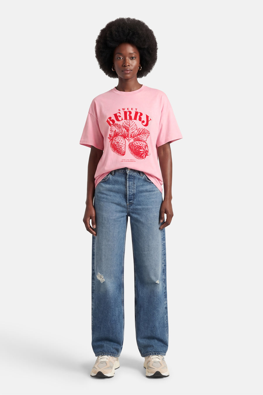 Roze T-shirt met korte mouwen van ONLY®, met een rode "Sweet Berry" opdruk en gedragen met blauwe jeans en crèmekleurige sneakers.
