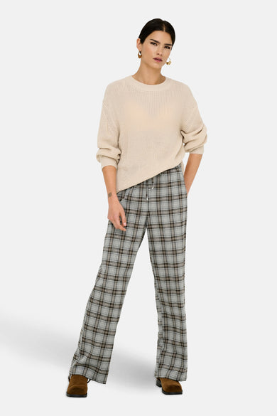 Pantalon gris de ONLY® avec un motif à carreaux, associé à une chemise beige tricotée et des chaussures marron.