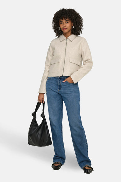 Ecru korte jas van ONLY, met zilverkleurige ritssluiting en opgestikte zakken, gecombineerd met blauwe jeans en zwarte ballerina's.
