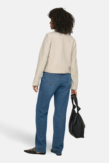 Ecru korte jas van ONLY, gezien van achteren, met lange mouwen, gecombineerd met blauwe jeans en zwarte handtas.

