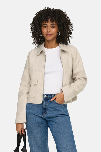 Ecru korte jas van ONLY, gedragen over een wit shirt en blauwe jeans.
