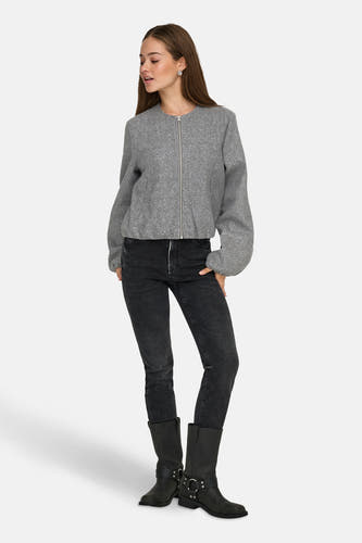 Grijze korte jas van JDY, met lange mouwen en een zilverkleurige ritssluiting, gecombineerd met een zwarte jeans en laarzen.