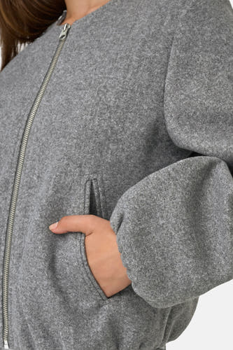 Grijze korte jas van JDY, met een zilverkleurige rits en steekzak, detailopname.