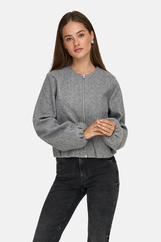 Grijze korte jas van JDY, met lange mouwen en een zilverkleurige ritssluiting, gedragen met een zwarte jeans.
