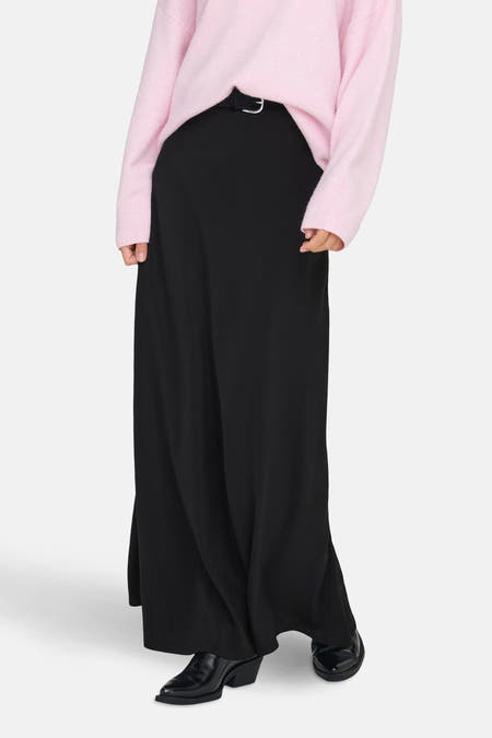 Lange zwarte rok van JDY, met een subtiele riem en gecombineerd met een roze trui en zwarte laarzen.
