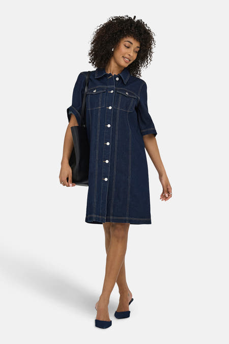 Donkerblauw denim kleedje met korte mouwen van JDY, met witte knopen en een zwarte tote bag.
