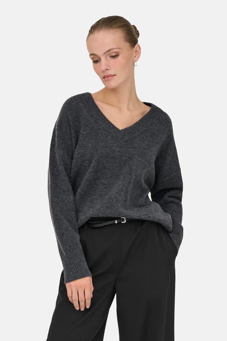 Grijze V-hals trui van ONLY, met lange mouwen, gecombineerd met een zwarte broek met riem.
