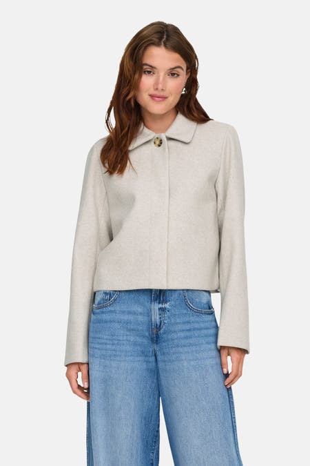 Korte ecru jas van ONLY, met lange mouwen en een kraag, gecombineerd met wijde jeans.
