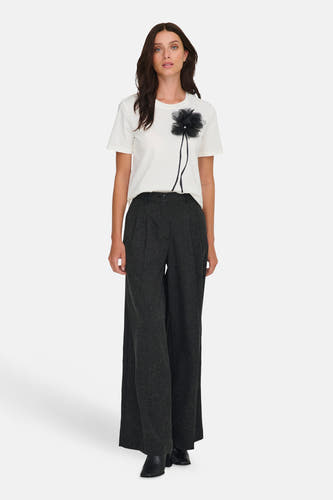 Grijze broek van JDY, met wijde pijpen en gedragen met een wit T-shirt met zwarte bloem applicatie.
