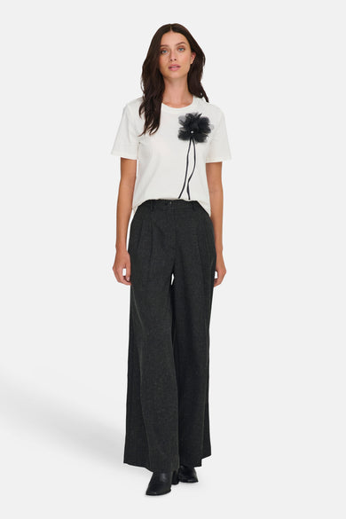 Grijze broek van JDY, met wijde pijpen en gedragen met een wit T-shirt met zwarte bloem applicatie.
