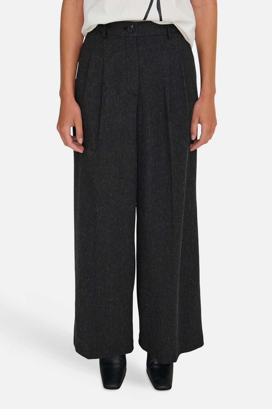 Een vrouw in een witte top en een wijde, donkergrijze pantalon.