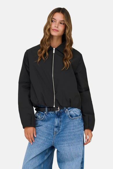 Veste courte noire de ONLY, avec une fermeture éclair argentée et portée avec un jean bleu et une ceinture noire.