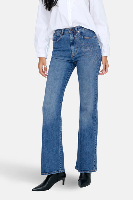 Middenblauwe flared jeans van ONLY, met versierde details op de zakken, gecombineerd met een witte blouse en zwarte laarsjes.
