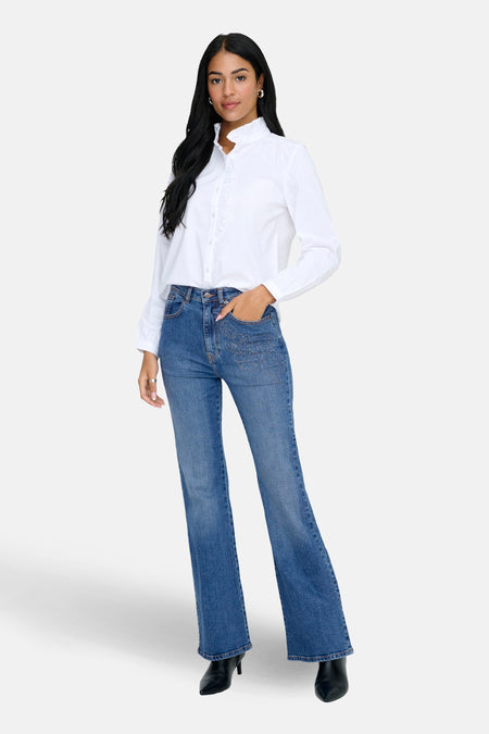 Middenblauwe denim flared jeans van ONLY met geborduurde details op de zakken, gecombineerd met een wit overhemd.
