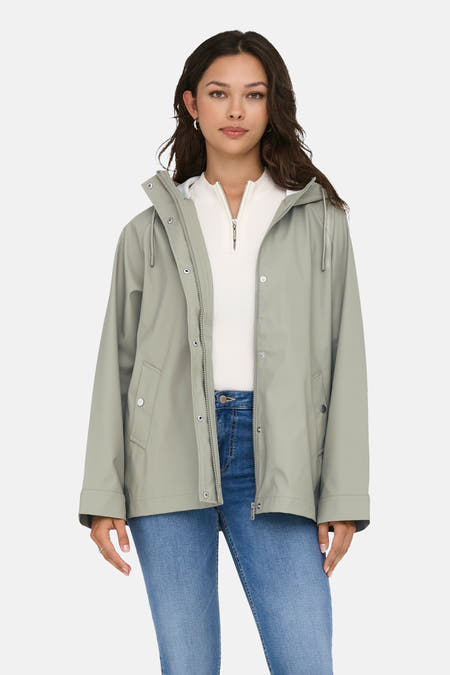 Kaki regenjas van ONLY met een capuchon, open gedragen over een witte trui en blauwe jeans.
