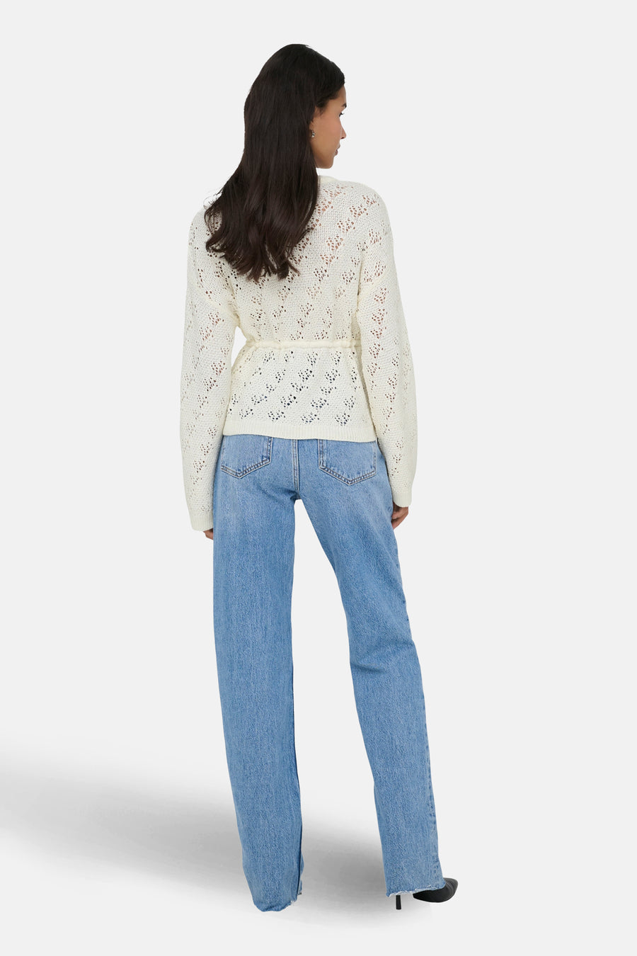 Achterkant van een vrouw in een beige vest en blauwe jeans op een witte achtergrond.