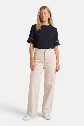Beige gekleurde jeans van JDY, met wijde pijpen en zichtbare stiksels, gedragen met een zwart shirt en witte sneakers.
