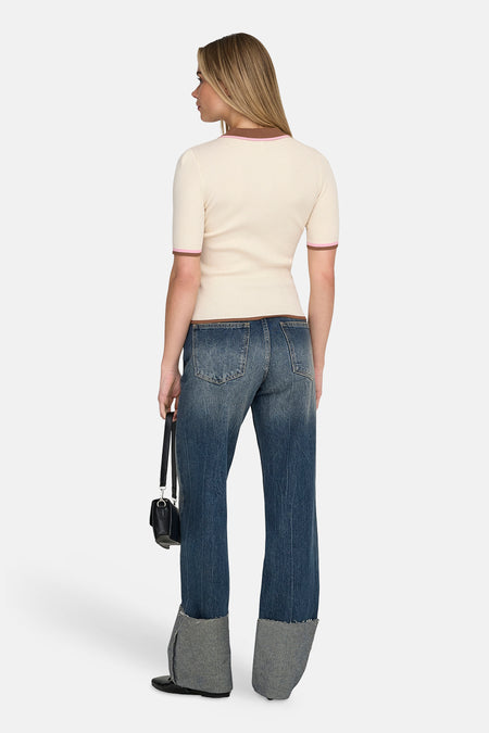 Polo écru à manches courtes de ONLY, avec des accents marron et rose, combinée avec un jean et un sac à main noir.
