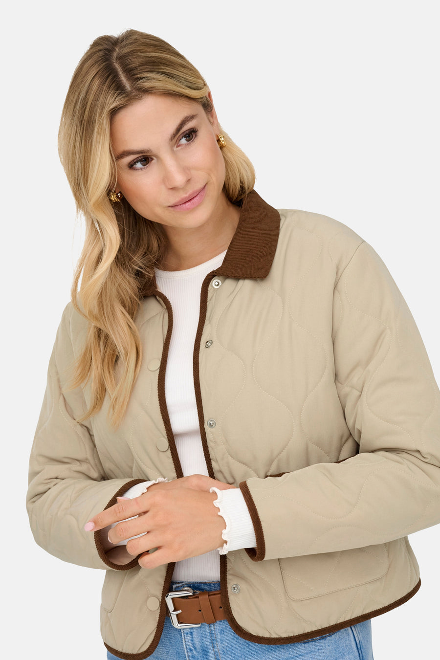 Beige korte jas van JDY, met bruine kraag en randen, gedragen over een witte top en blauwe jeans.
