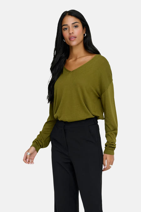 Groene trui met V-hals van JDY, met lange mouwen en gedragen met een zwarte pantalon en zilveren sieraden.
