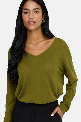 Pull vert avec col en V de JDY, à manches longues et porté avec un pantalon noir et des boucles d'oreilles argentées.