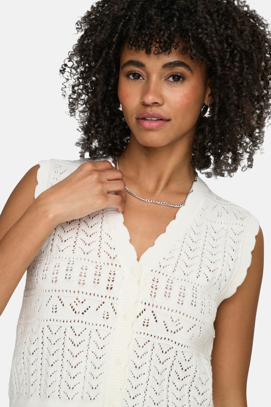 Wit gilet van ONLY® met gehaakt ajourpatroon, geschulpte V-hals en knoopsluiting, gedragen door een model met zilveren ketting.