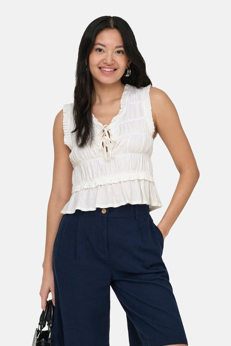 Chemisier blanc sans manches de ONLY, avec volants et laçage, combiné avec un pantalon bleu marine.