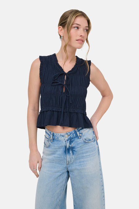 Chemisier bleu sans manches de ONLY, avec volants et fermeture à nœud, combiné avec un jean ample et des talons.