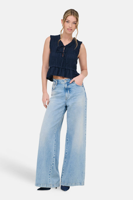 Mouwloze blauwe blouse van ONLY, met ruches en een striksluiting, gecombineerd met wijde jeans en hakken.
