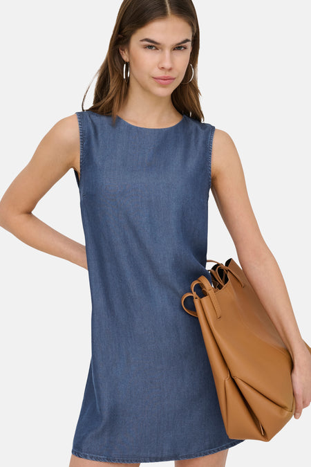 Robe sans manches en jean bleu foncé de ONLY®, portée par un mannequin avec un sac à main marron.