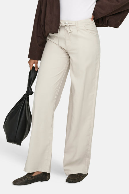 Jean de couleur écru de ONLY®, combiné avec un t-shirt blanc et une veste marron, avec une main dans la poche.