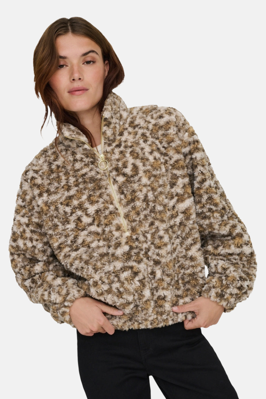 Beige fleece jas van ONLY®, met een bruin en wit vachtpatroon, korte ritssluiting en zwarte broek.
