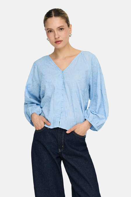 Blauwe blouse met lange mouwen van ONLY, versierd met een subtiel bloempatroon, gedragen met donkere jeans.
