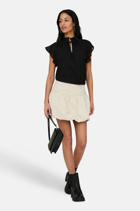 Korte ecru rok van ONLY, met een geplooid ontwerp en gedragen met een zwarte top en laarzen.
