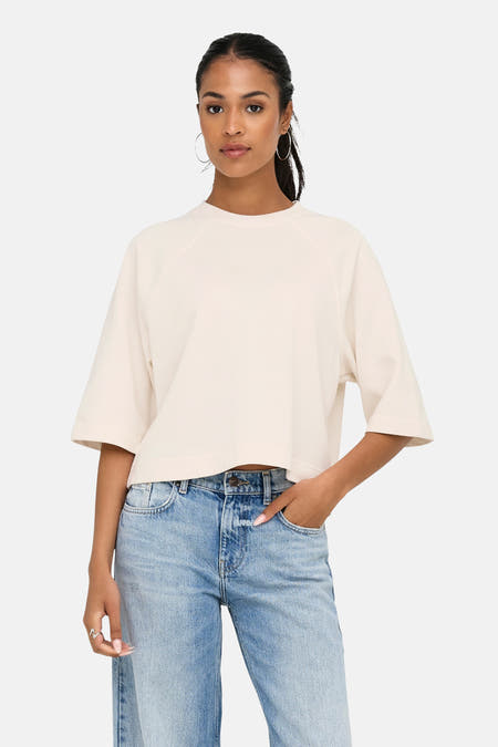 Ecru T-shirt met korte mouwen van ONLY, gedragen met een jeans met wijde pijpen en zilveren oorringen.
