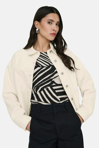 Ecru korte jas van JDY, met lange mouwen en knoopsluiting, gecombineerd met een zwart-wit zebraprint top en zwarte broek.