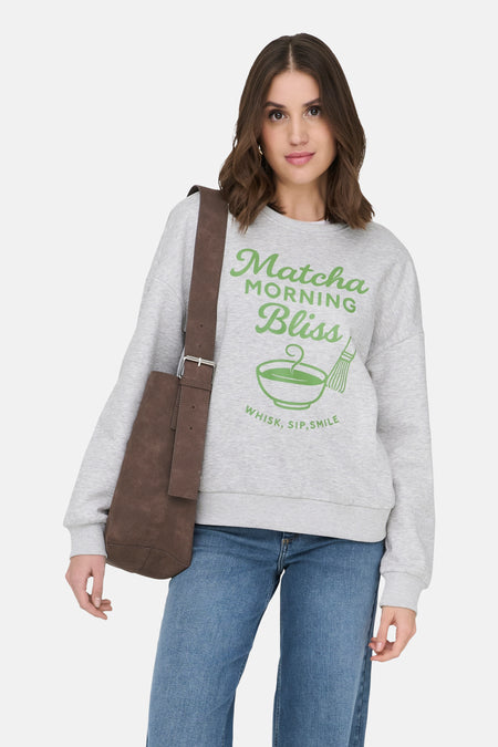 Grijze sweater van ONLY, met een groene "Matcha morning bliss" opdruk en een model met een bruine tas over haar schouder.
