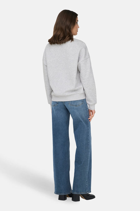 Grijze sweater met ronde hals van ONLY, losse pasvorm, gecombineerd met blauwe jeans en zwarte hakken, achteraanzicht.
