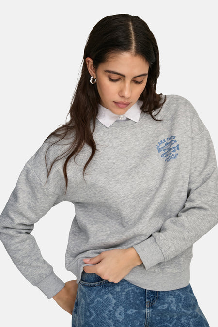 Grijze sweater van ONLY met een blauwe opdruk en een witte blouse eronder, gecombineerd met een blauwe jeans.