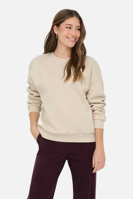 Ecru sweater met ronde hals van ONLY, gedragen met bordeauxrode broek en zilveren oorbellen.