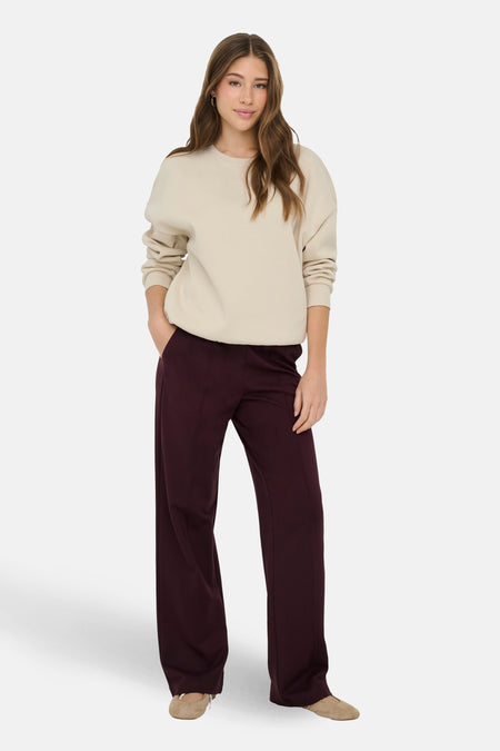 Ecru sweater van ONLY, met lange mouwen, gedragen met bordeauxrode broek en platte schoenen.